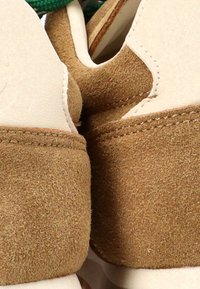 Acercamiento de zapatillas de ante marrón y cuero blanco con costuras visibles y cordones verdes.