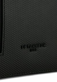 Borsa in pelle nera testurizzata con un motivo geometrico, caratterizzata da un logo impresso "Le Tanneur 1898" sulla superficie.