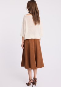 Kremowy sweter z krótkim rękawem, połączony z brązową zamszową spódnicą midi i szpilkami w leopardzi wzór. Skupienie na teksturze i kontraście kolorów.