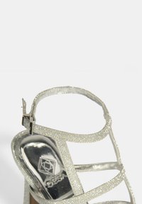 Silberner Glitzer-Sandale mit hohen Absätzen, metallischem Finish, verstellbarem Knöchelriemen und glänzender Sohle mit Markenlogo-Detail.