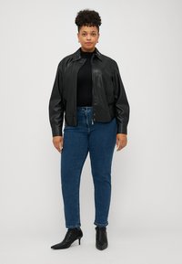 Black leather jacket with a relaxed fit, zip closure, and ribbed cuffs, paired with dark blue straight-leg jeans and black ankle boots.