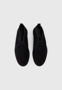 Scarpe nere in suede con punte rotonde, lacci minimal e tasselli sul tallone a cerchio. Presentano una texture liscia e bordi cuciti per una maggiore durata.