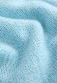 Tissu en tricot bleu clair doux, avec des coutures visibles et de légers plis créant une surface texturée et des ombres subtiles.