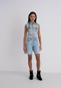 Denim jaka ar saīsinātu dizainu, gaišā mazgājumā, ar pogām, kombinēta ar gaiši ziliem denim šortiem. Modelis valkā melnus potīšu zābakus.