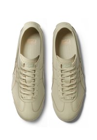 Beige Sportchuhe aus glattem Leder, rundem Zehenbereich, sechs Schnürlöchern und dezenten Nähdetails. Branding auf der Zunge und der Ferse.