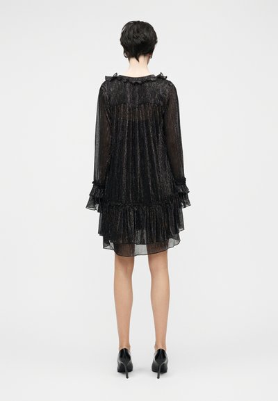 Μαύρο, βολβοειδές, διαφανές φόρεμα με γυαλιστερές μεταλλικές κλωστές, μακριά μανίκια και σχεδιασμό με πολλαπλές φάσες στο τελείωμα. Συνδυάζεται με μαύρα ψηλοτάκουνα παπούτσια.