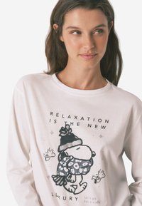 Witte longsleeve shirt met een zwart graphic van een hond in een hoed en sjaal, met tekst erboven en eronder in zwart, op een gladde katoenen stof.