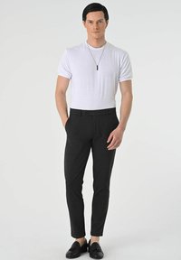 Black tailored trousers with a smooth texture, paired with a white short-sleeve t-shirt. Accessories include a thin black pendant necklace.