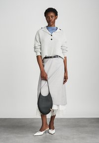 Lichtgrijze geribbelde trui met capuchon, zwarte riem, grijze midi-rok met kant, zwarte tas en witte puntige hakken. Eenvoudig en modern ontwerp.