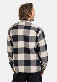 Men's flannel shirt featuring black and cream checkered pattern, buttoned cuffs, a classic collar, and a relaxed silhouette. Textured fabric.