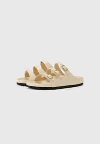 Beige sandaler med tre justerbare stropper, gullbelagte spenner og en formet fotseng. Svarte gummisåler for godt grep. Glatt tekstur.