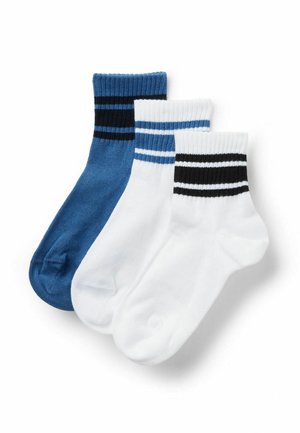 Trzy skarpetki do kostek: jedna niebieska z czarnymi paskami, dwie białe z niebieskimi lub czarnymi paskami na prążkowanych mankietach, ułożone nachodzące na siebie na białym tle.
