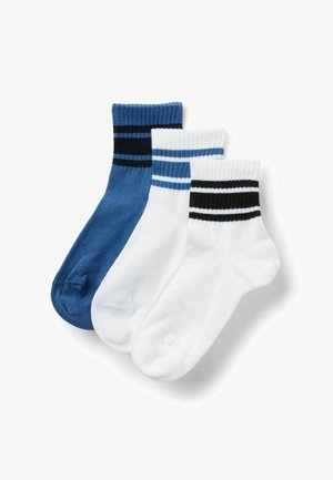 Trois chaussettes basses : une bleue avec des rayures noires, deux blanches avec des rayures bleues ou noires sur des bords côtes, disposées en chevauchement sur fond blanc.