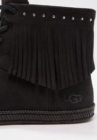Botte de cheville en suède noir avec des franges, des clous argentés sur le dessus, et une semelle en caoutchouc noir texturée avec des bords tissés.