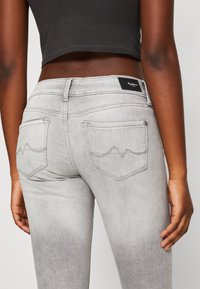 Grå denimjeans med en medelhög midja, kontrasterande sömmar, två bakfickor med vågmönster och en varumärkesetikett.