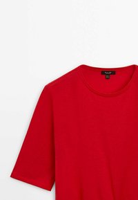T-shirt rossa a maniche corte realizzata in tessuto morbido, con scollatura a girocollo e design a taglio dritto. L'etichetta mostra le informazioni sulla taglia.
