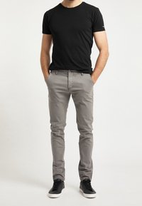 Grå bomulds chinos med slim fit, der har sidelommer og knaplukning, parret med en tætsiddende sort bomulds t-shirt og sorte sneakers.