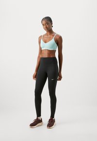 Light blue sports bra with thin straps, paired with high-waisted black leggings featuring a small white Nike logo. Brown athletic shoes.