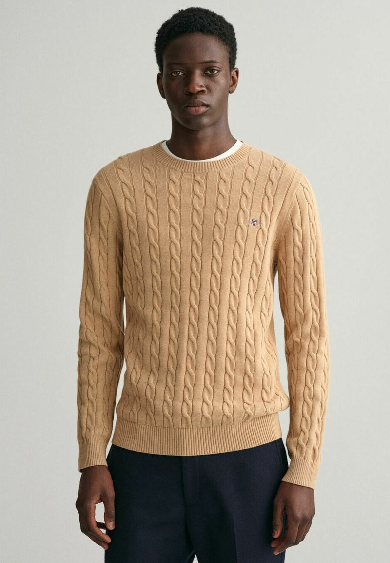 Beige Kabelstrickpullover mit strukturiertem Design, rundem Halsausschnitt und gerippten Bündchen und Saum, mit kleinem Logo auf der Brust.