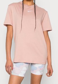 Rosa Nike t-shirt med kort ärm och rund halsringning, prydd med en vit logga. Matchas med ljusmönstrade shorts i pastellfärger.