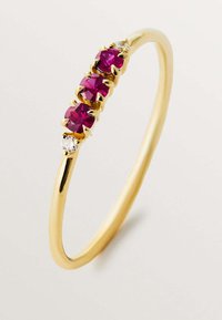 Anillo de oro con tres piedras pink redondas y facetadas, con un pequeño acento de diamante, montado en una banda lisa y delgada.