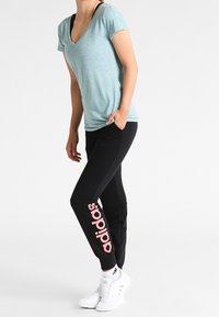 Vaaleansininen v-kauluspaita lyhyillä hihoilla, yhdistettynä mustiin verkkareihin, joissa on vaaleanpunainen "adidas"-logo ja valkoiset urheilukengät.