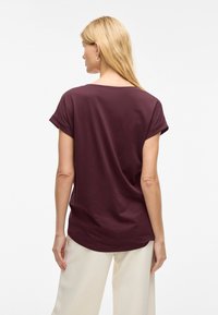 Bordo kratka majica s kratkimi rokavi in sproščenim krojem, okroglim izrezom in zavihanimi manšetami, kombinirana z zasenčenimi, ohlapnimi hlačami.