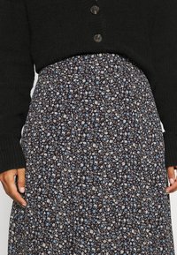 Cárdigan de punto negro con tres botones, combinado con una falda de estampado floral con fondo marino y pequeñas flores azules y beiges.
