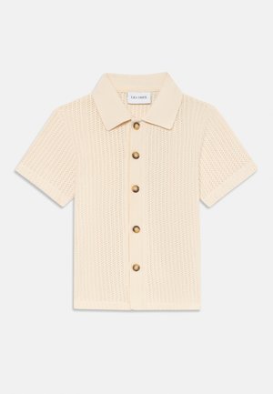 Short-sleeved, cream knit polo shirt with a textured pattern, featuring a classic collar and five large round buttons on the front.