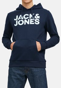 Marineblauwe hoodie van katoen, met een voorzak, een trekkoordcapuchon en grote witte tekst "JACK & JONES" over de borst.