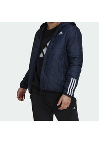 Námořnicky modrá vatovaná bunda s kapucí, prošívaným designem, předním zipem a bílými třemi pruhy na rukávech. Zobrazená černá vnit řní vrstva.