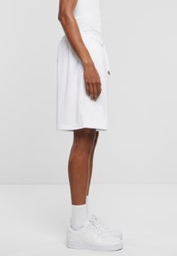 Hvite mesh treningsshorts med elastisk midje, sidelommer og løs passform, kombinert med hvite treningssko og sokker.