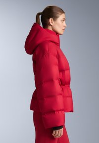 Piros steppelt téli kabát kapucnival, dobozszerű szabással, steppelt mintázattal és elasztikus derékrésszel. Simább, fényes felületű anyagból.