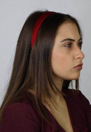 Czerwona satynowa opaska na głowę noszona przez osobę o długich brązowych włosach. Tło jest neutralne, co podkreśla kolor i fakturę opaski.