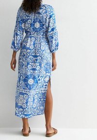 Largo vestido azul con patrones florales blancos, con mangas tres cuartos y una abertura en el costado, hecho de una tela ligera.