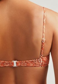 Top de bikini naranja con un patrón de cachemira, con tirantes finos y cierre de gancho, que muestra una textura suave contra la piel.