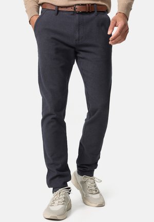 Navy slim-fit trousers made of textured fabric, featuring side pockets and a brown leather belt, paired with beige sneakers.