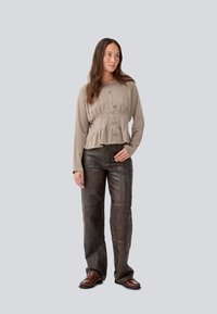 Bluză peplum bej cu nasturi, asortată cu pantaloni din piele maro închis cu un finisaj texturat și cusături vizibile. Pantofi maro completează look-ul.
