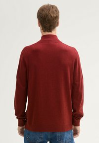 Rot gestrickter Pullover mit Stehkragen, langen Ärmeln, gerippten Bündchen und Saum. Der Stoff hat eine weiche Textur und ein leicht meliertes Aussehen.