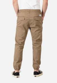 Pantalones jogger beige con cinturilla elástica, puños en los tobillos y dos bolsillos traseros. Combinados con zapatillas negras con suelas blancas.