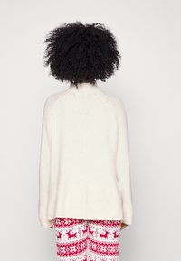 Maglione lavorato a maglia color crema con maniche raglan e orlo a coste. Abbinato a pantaloni del pigiama festivi a strisce rosse e bianche con renne.