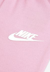 Ροζ βαμβακερό ύφασμα με ραβδωτή υφή, με ένα μεγάλο λευκό λογότυπο Nike τοποθετημένο σε περίοπτη θέση στο κέντρο.