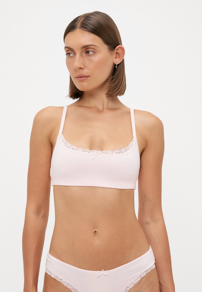Roze bralet s čipkastim detaljima, podešavanim trakama i prednjim mašnom. Mekana tkanina pruža glatku teksturu, nudeći minimalistički dizajn.