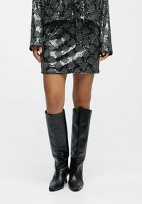 Robe noire à sequins avec un corsage ajusté et des manches amples. Bottes en cuir noir montantes jusqu'au genou avec un bout pointu et un léger talon.