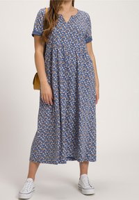 Blå blommig maxiklänning med korta uppvikta ärmar, V-ringning, samlad midja och längd som når mitt på vaden. Matchad med vita sneakers.