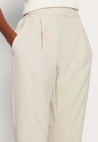 Beiga skräddarsydda byxor har en veckad design, sidofickor och en slät yta, vilket gör dem lämpliga för mångsidig styling.