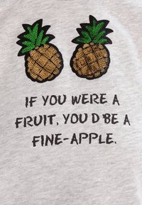 Camiseta gris con dos piñas de lentejuelas doradas y verdes sobre el texto impreso: "SI FUERAS UNA FRUTA, SERÍAS UNA PIÑA FINA."