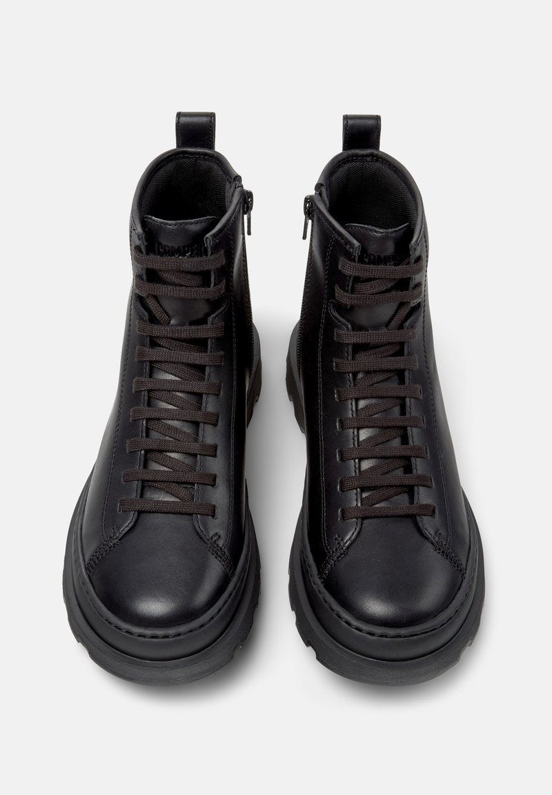 Zwarte leren hoge laarzen met dikke zolen, voorveters en zijritsen op een witte achtergrond, van bovenaf bekeken.