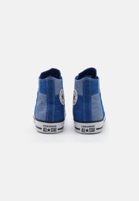 Niebieskie wysokie trampki wykonane z denimu, z kontrastowym jasnoniebieskim panelem, czarno-białą podeszwą oraz okrągłym emblematem marki na pięcie.