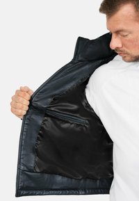 Giubbotto di pelle blu navy con un'esterno liscio, chiusura frontale con cerniera e un interno in satin nero caratterizzato da una piccola tasca con cerniera.